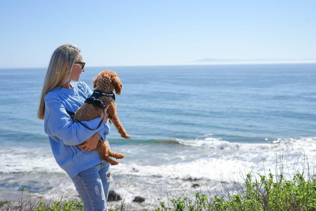 A young woman holding her small dog, looking out at the ocean, on the Carpinteria Bluffs Trail.